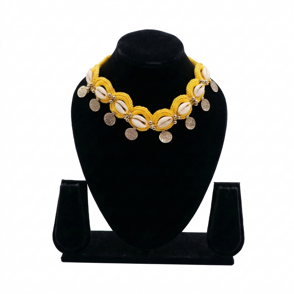 Yellow crochet choker necklace featuring white cowrie shells and hanging silver engraved coins on a black display stand.