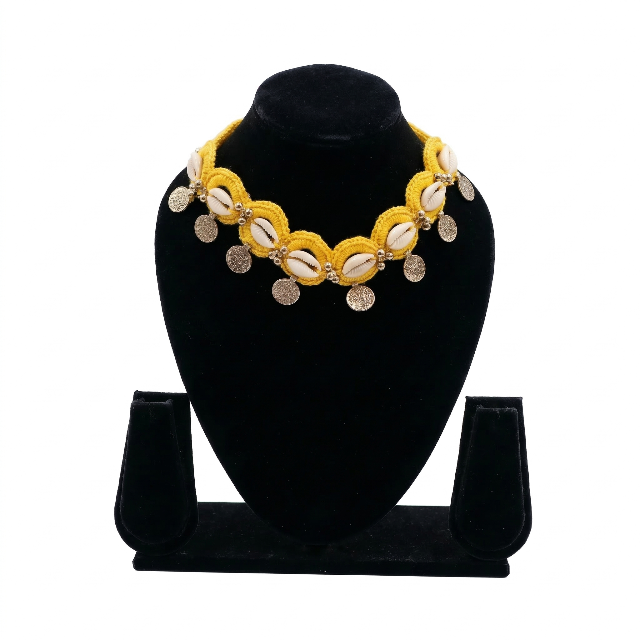 Yellow crochet choker necklace featuring white cowrie shells and hanging silver engraved coins on a black display stand.
