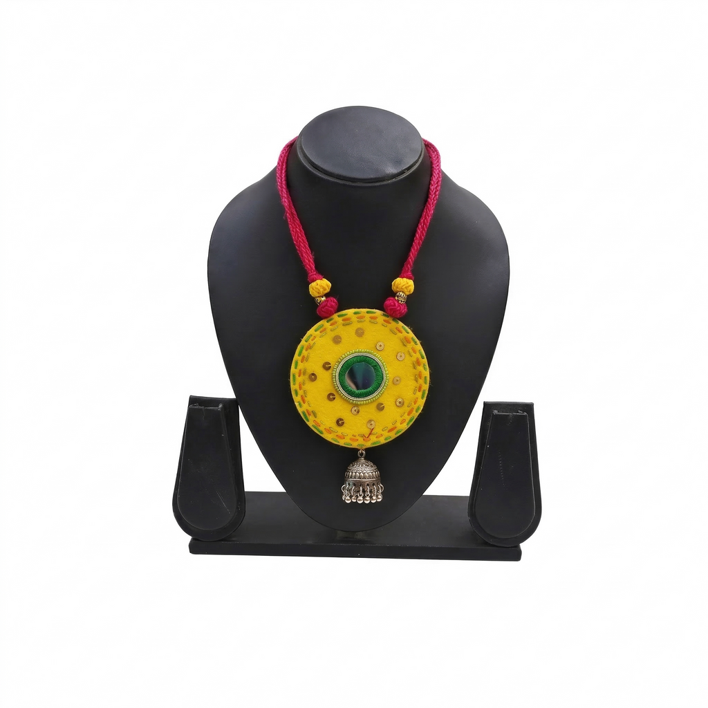 Handcrafted yellow fabric pendant necklace featuring green mirror work, pink thread cord, and a silver oxidised jhumka hanging.