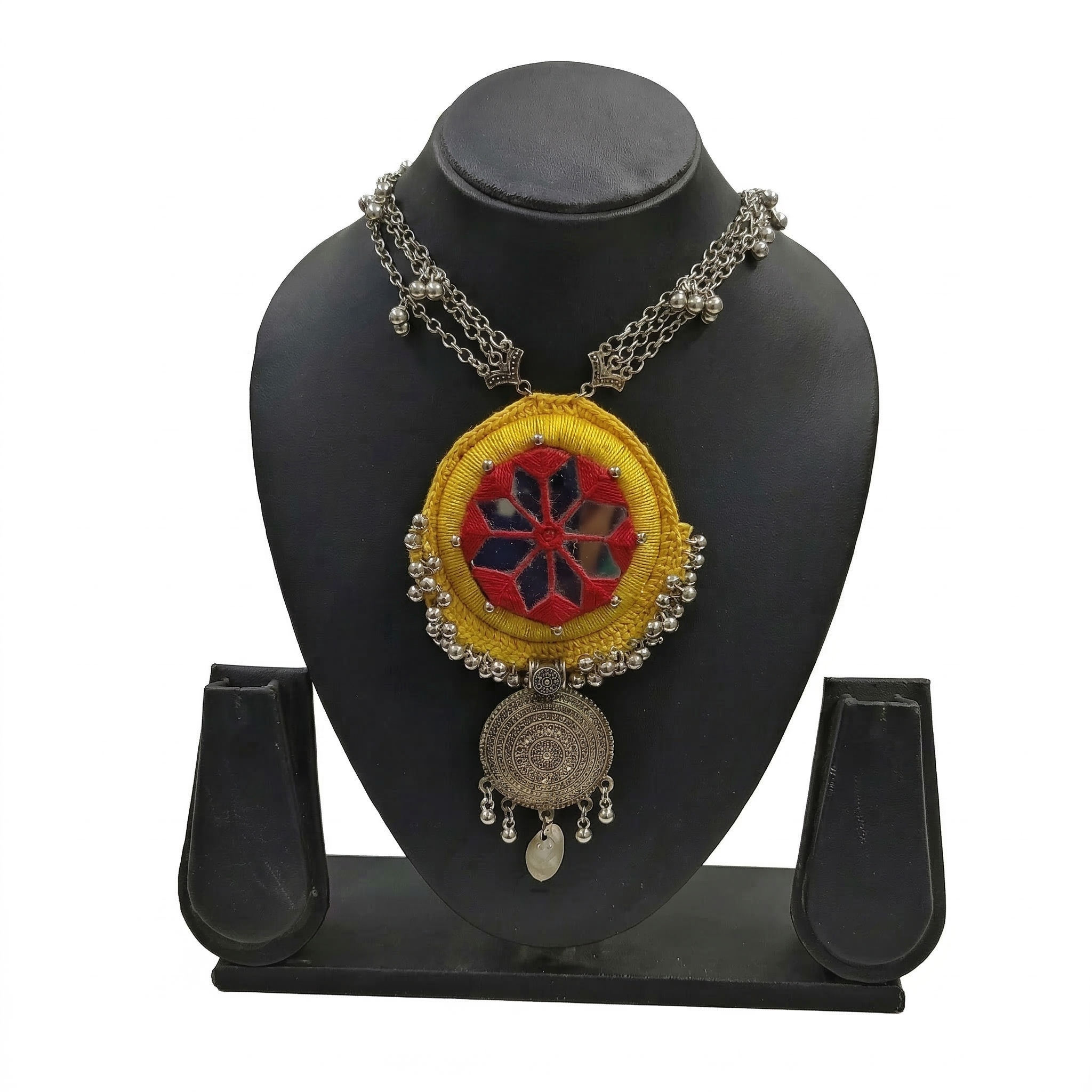 Handmade yellow fabric necklace with red mirror work embroidery and silver oxidized mandala pendant on a black display stand.