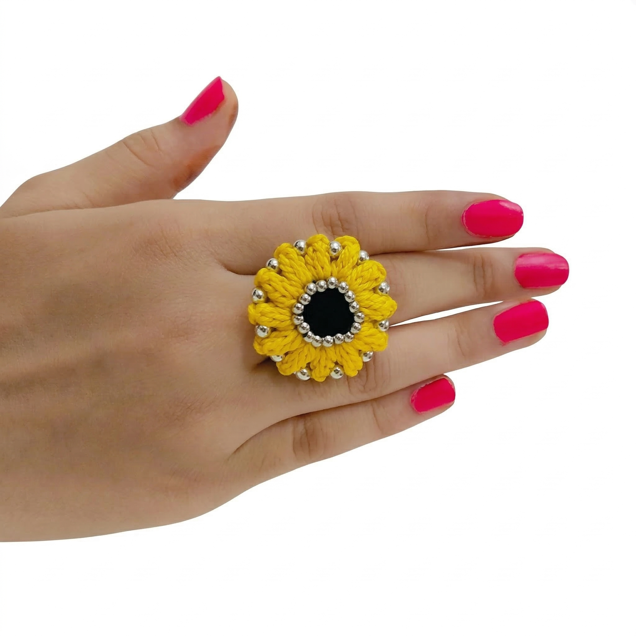 A hand wearing a large yellow crochet sunflower ring with a black center and silver beads on a white background.
