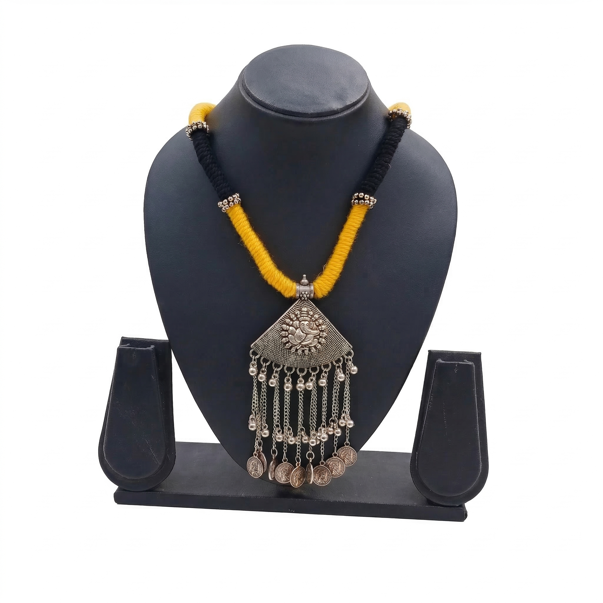 Oxidized silver Ganesha pendant necklace on yellow and black silk thread cord with hanging metallic charms, displayed on a black jewelry stand.