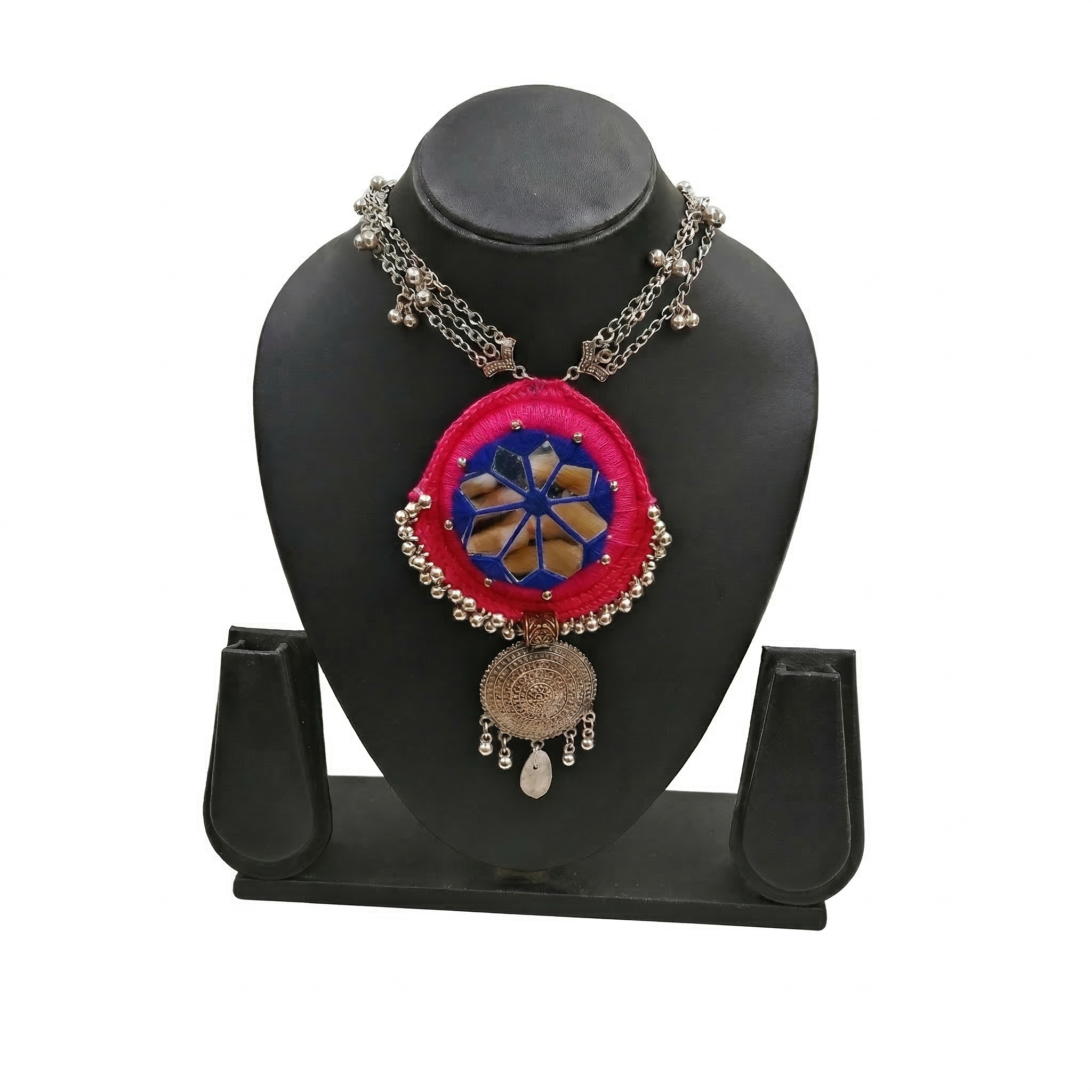 Pink handcrafted fabric necklace with blue mirror work and silver oxidized circular pendant on a black display stand.