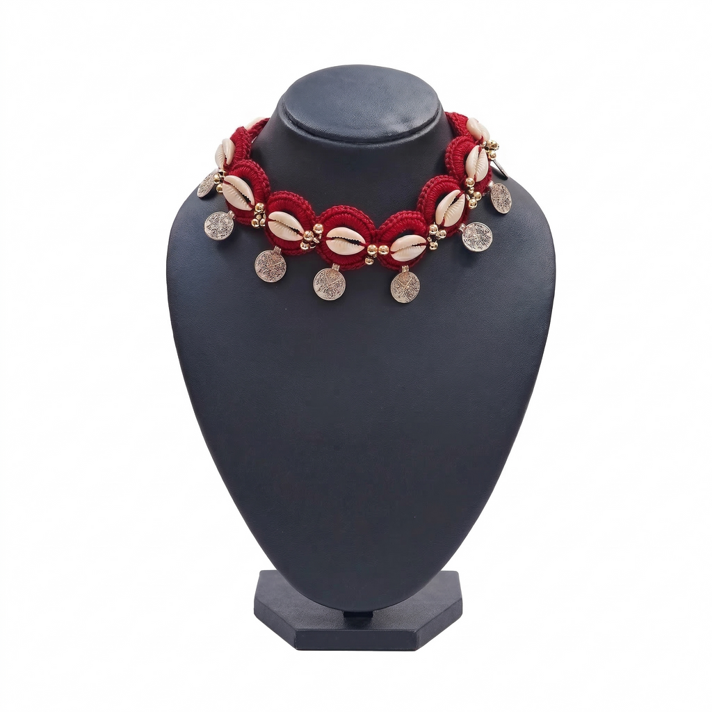 Red handmade crochet choker necklace featuring white cowrie shells, gold beads, and dangling silver-tone coin charms on a black display stand.