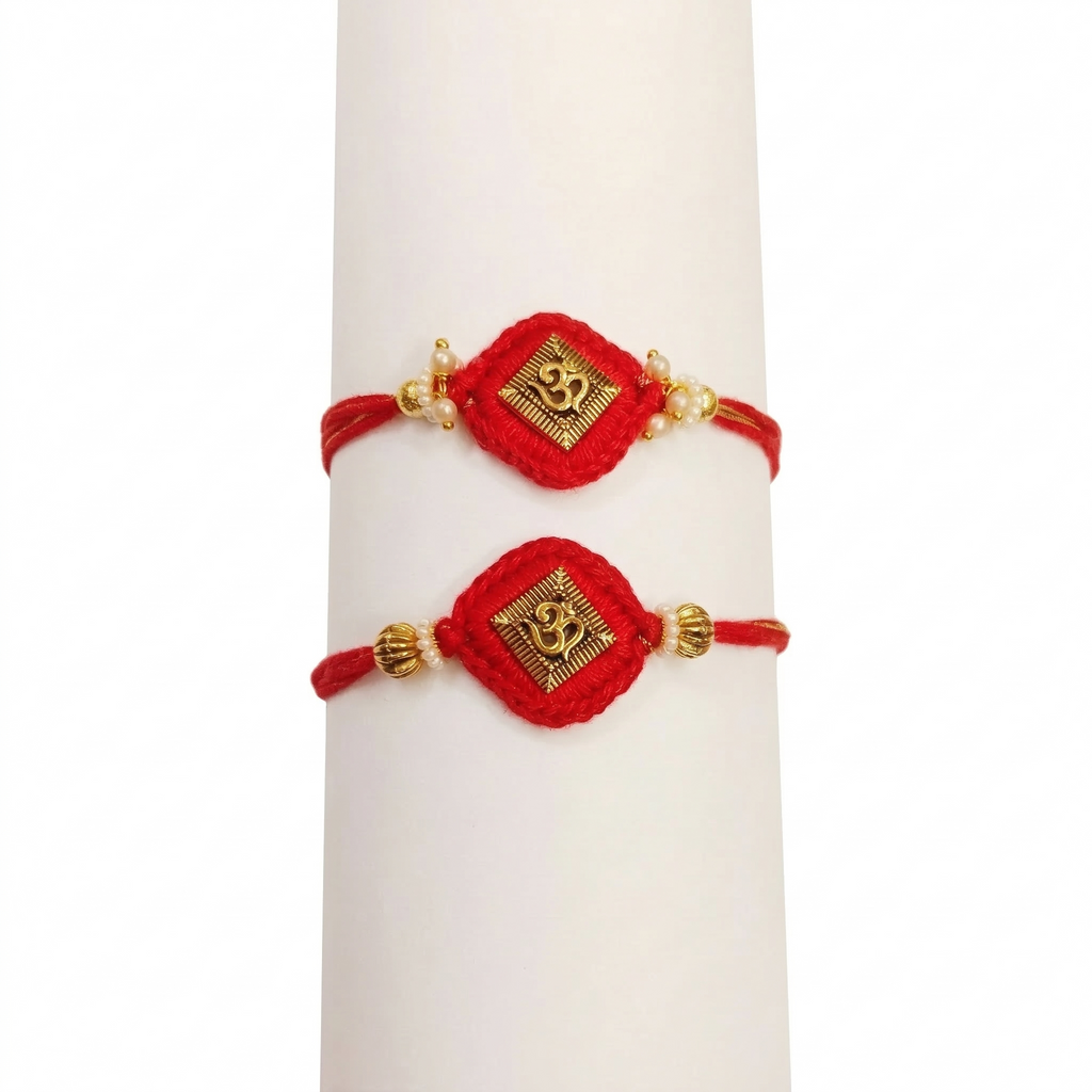 Pair of traditional red thread Rakhis with gold Om charms and pearls on a white display stand.