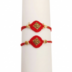 Pair of traditional red thread Rakhis with gold Om charms and pearls on a white display stand.