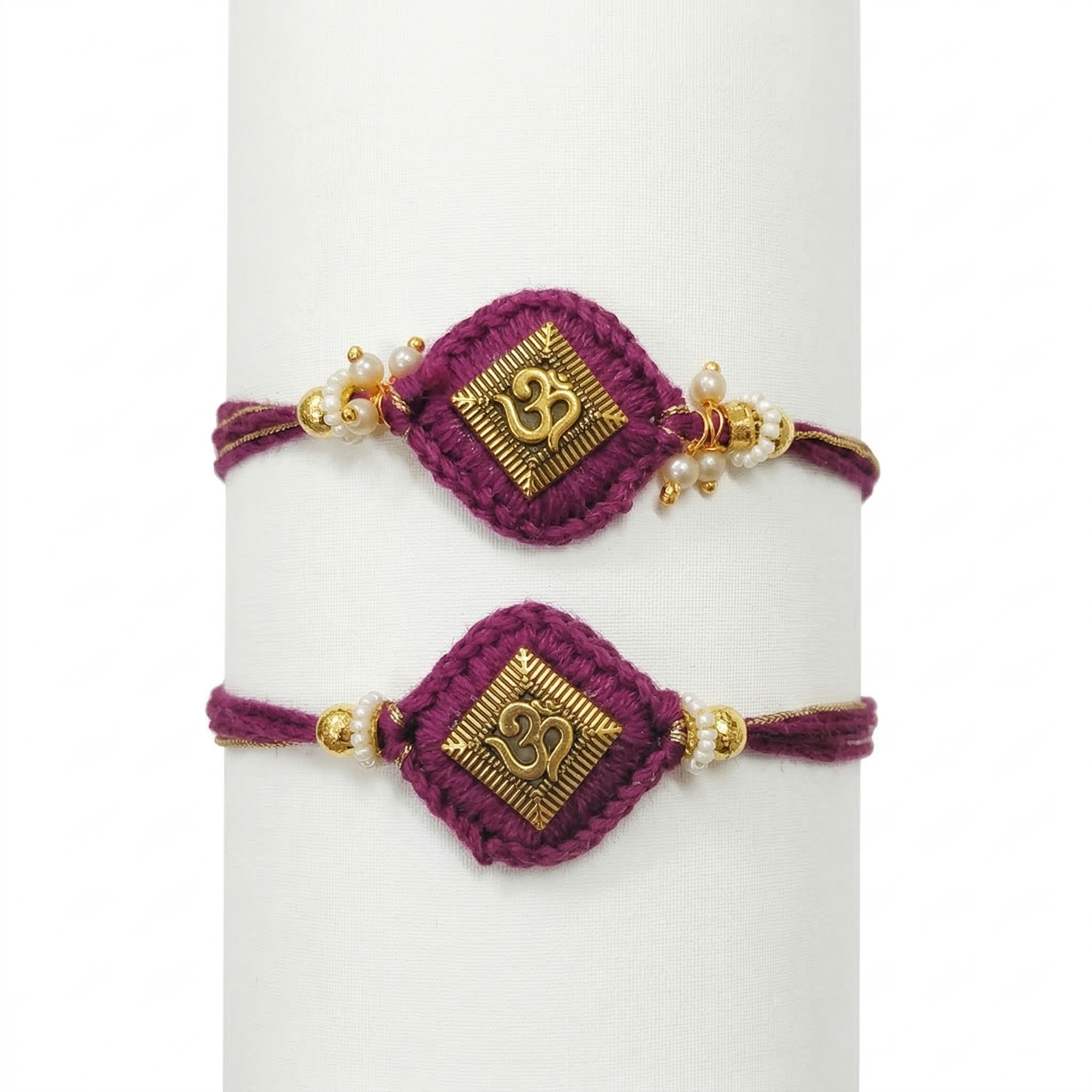 Two handcrafted purple thread Rakhis featuring gold-toned Om emblems on diamond-shaped crochet bases with pearl and gold bead embellishments.