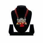 Handcrafted oxidized silver pendant necklace featuring peacock motifs, red multi-strand thread, and vibrant red and yellow pom-pom tassels on a display stand.